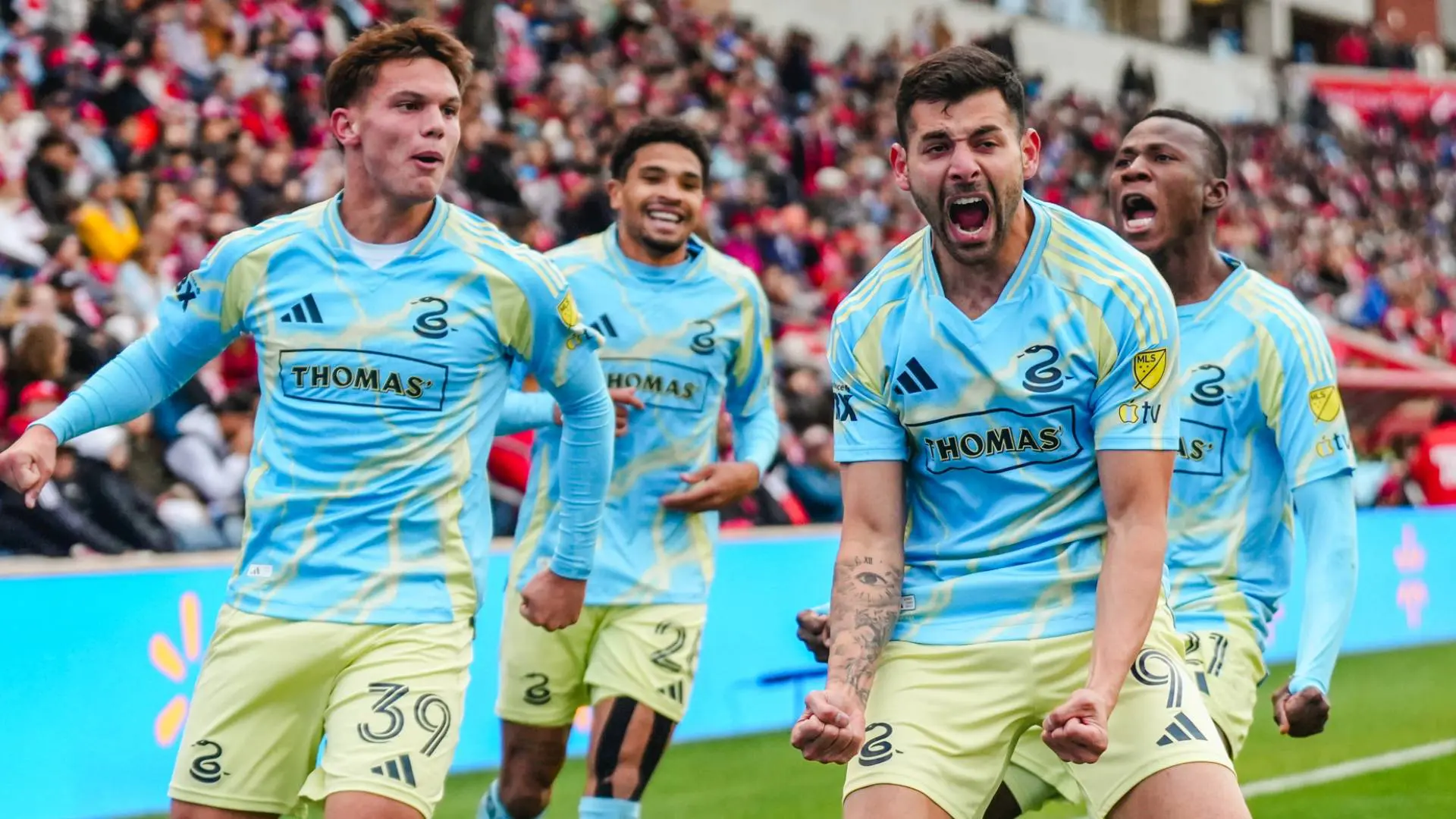 Philadelphia Union forward Tai Baribo screams in celebration after scoring a goal, surrounded by teammates in their blue and yellow away kits during an MLS playoff match against Chicago Fire.