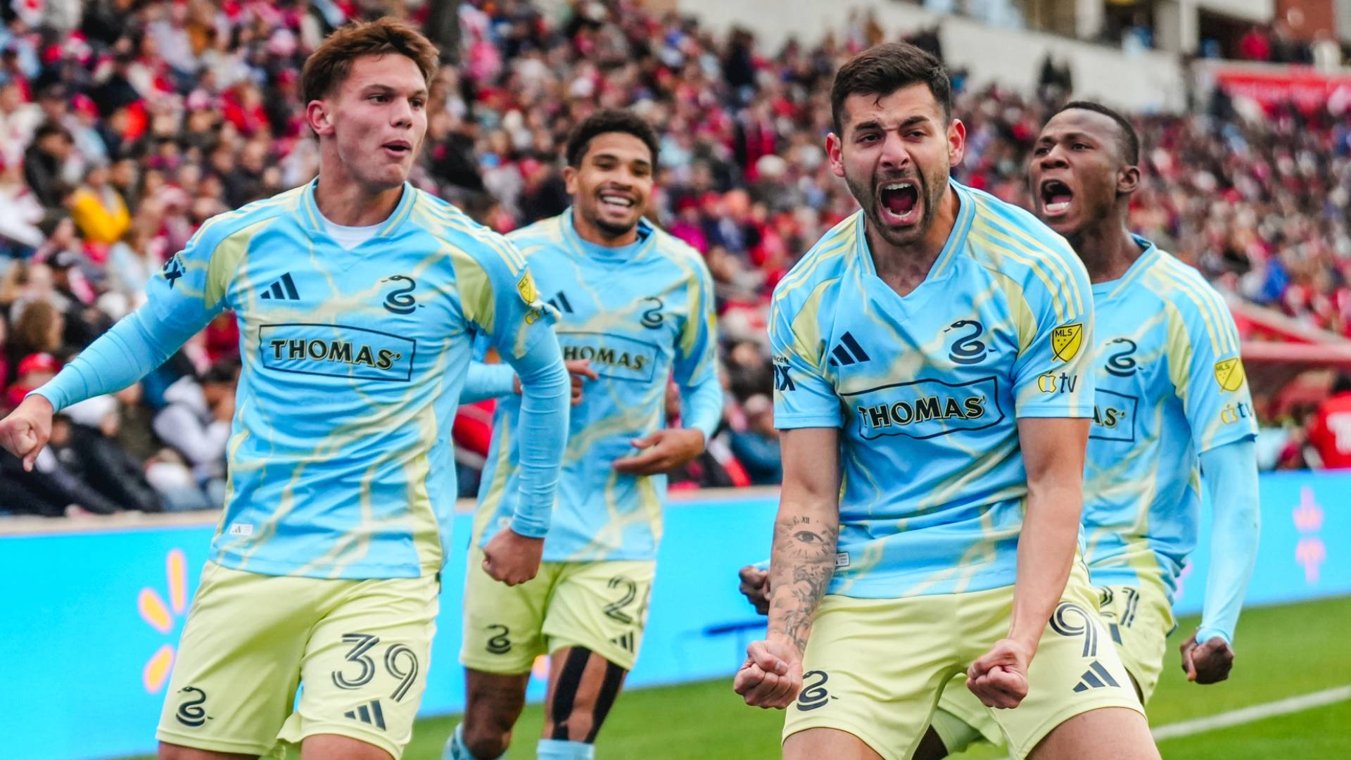 Philadelphia Union forward Tai Baribo screams in celebration after scoring a goal, surrounded by teammates in their blue and yellow away kits during an MLS playoff match against Chicago Fire.